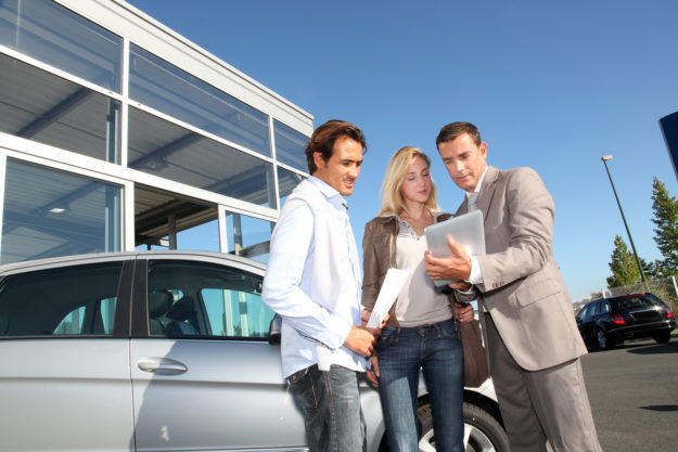 Car seller with couple looking at electronic tablet Service at a car dealership