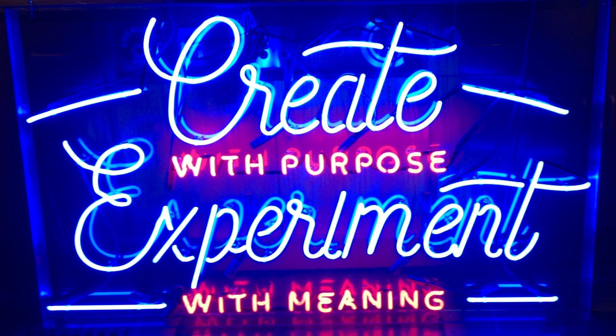 neon sign says create purpose experiment meaning