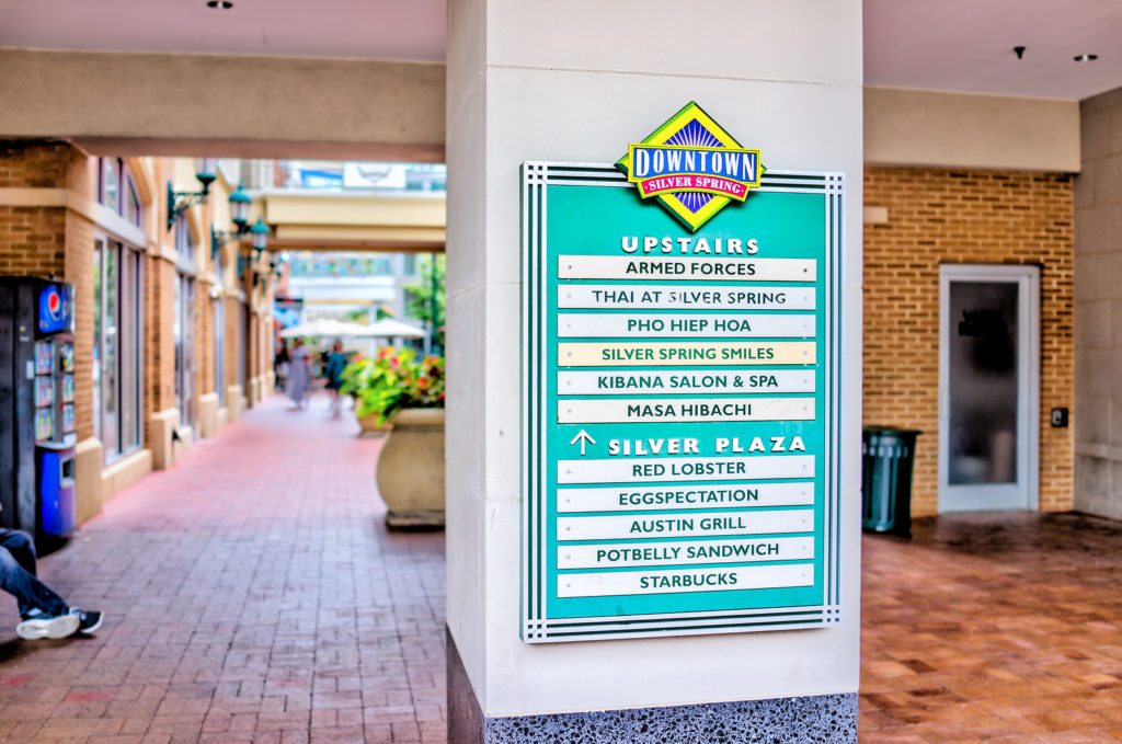 Downtown area of city in Maryland with large directional sign on shopping mall building and directions for restaurants and shops