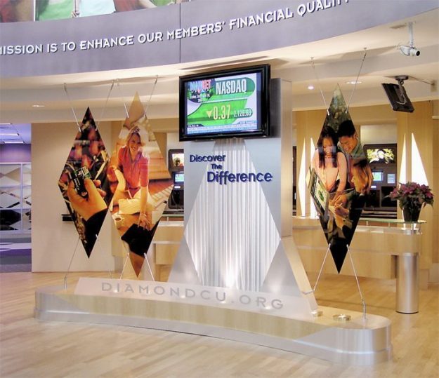 Diamond Credit Union Digital Signage A large and vibrant digital display displaying “NASDAQ” is situated at the center of the interior lobby of a financial institution.