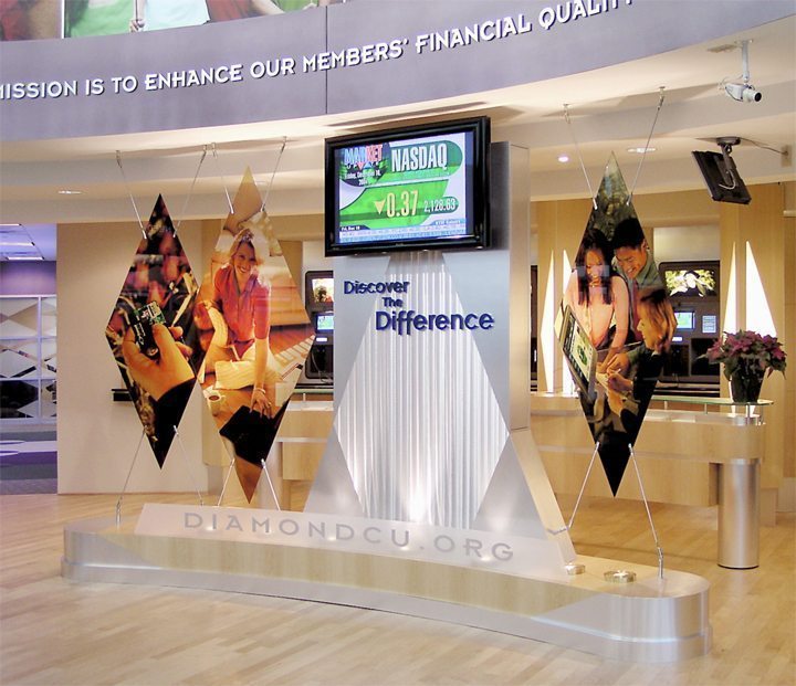 Diamond Credit Union Digital Signage A large and vibrant digital display displaying “NASDAQ” is situated at the center of the interior lobby of a financial institution.